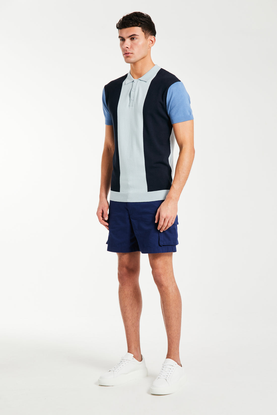 Side profile of model wearing block men's knitted polo in blue and shorts