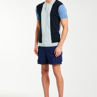 Side profile of model wearing block men's knitted polo in blue and shorts