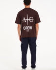 Backshot of model wearing brown crew neck T-shirt with large Avant Garde logo on the reverse