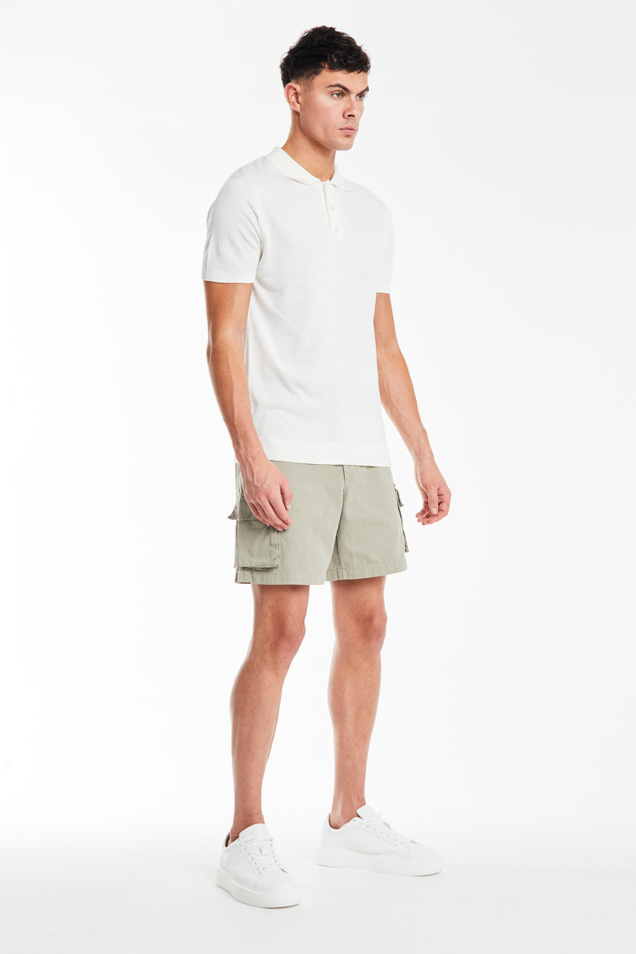 side profile of sage green men's utility shorts styled with a polo