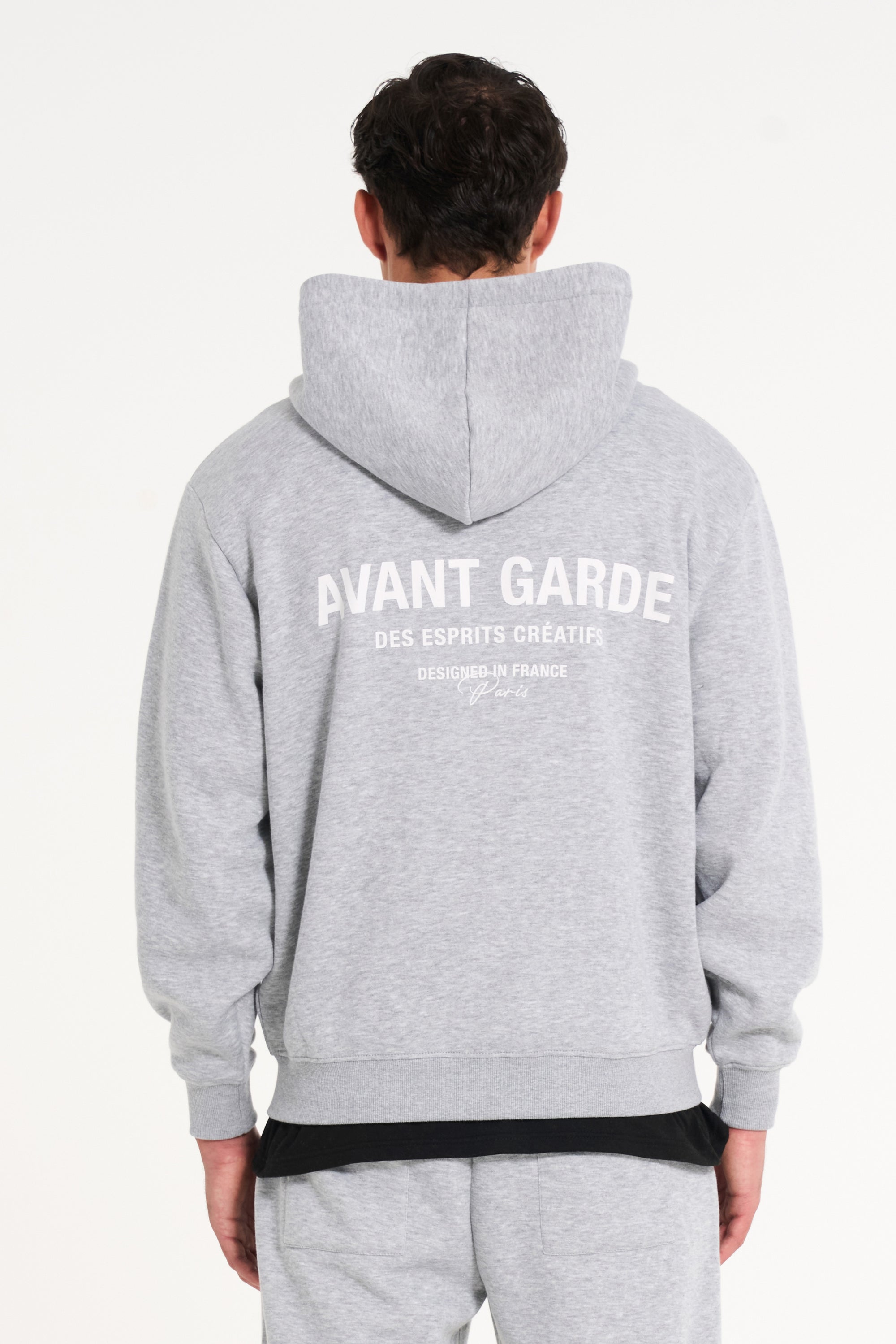 Backshot of model wearing grey zip up hoodie with Avant Garde writing across the back