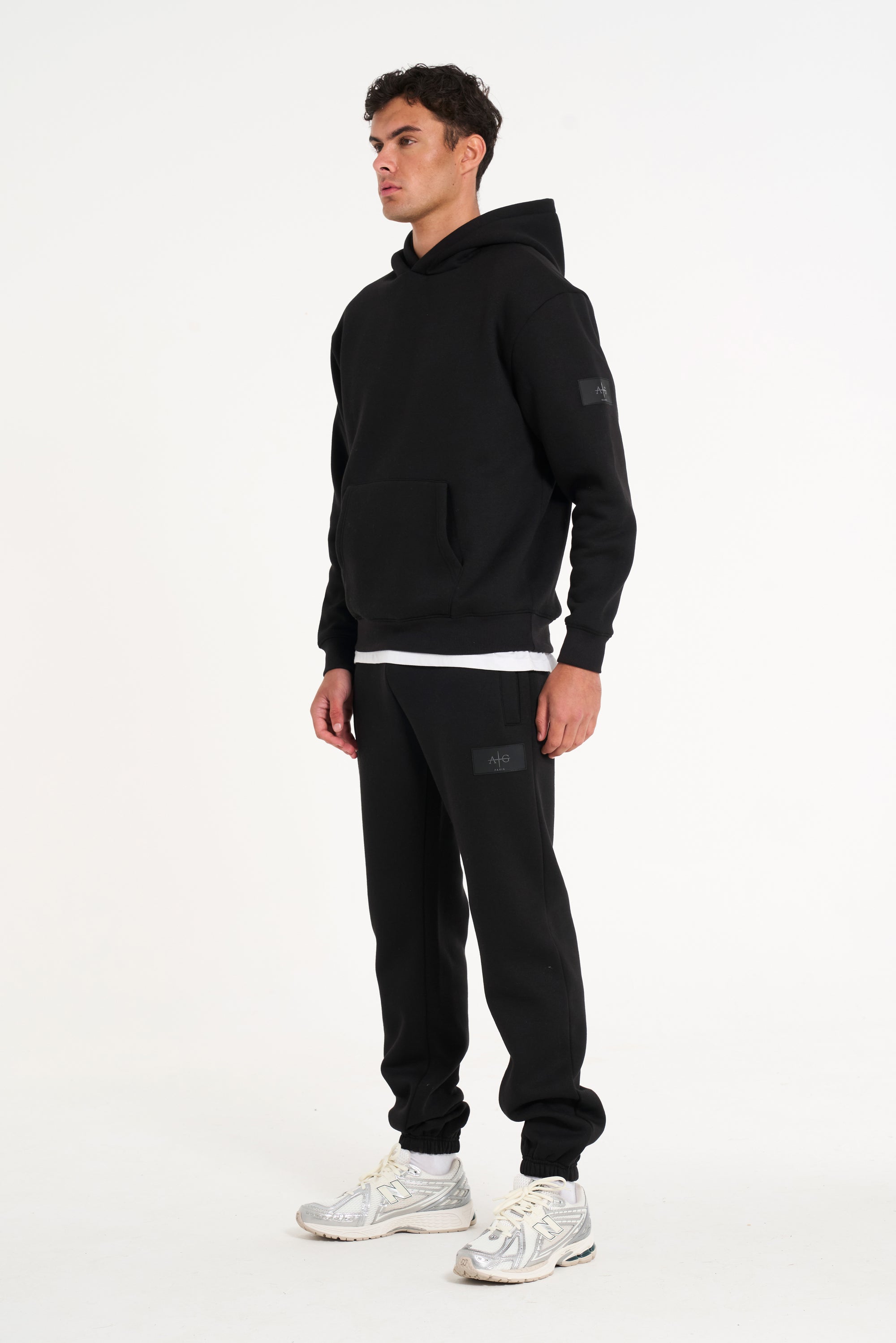 Model wearing full black tracksuit with badge logo on arm and bottoms