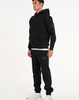 Model wearing full black tracksuit with badge logo on arm and bottoms