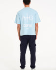 Backshot of man wearing sky blue T-shirt with large Avant Garde logo on the back