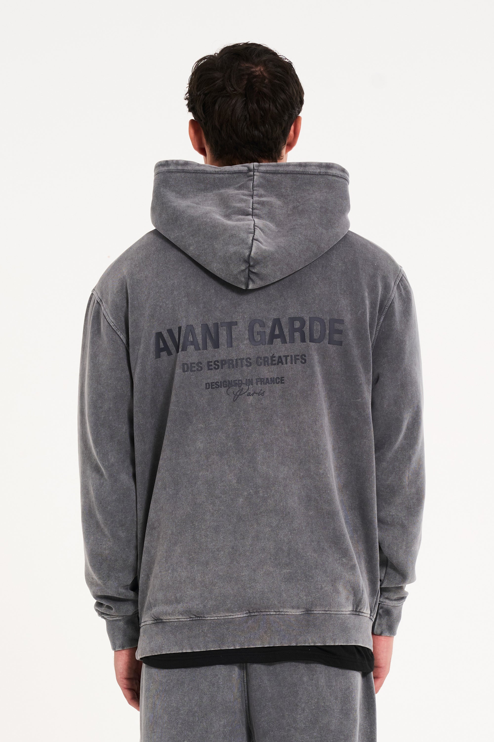 Model facing away from the camera wearing men's hoodie with Avant Garde writing on the back