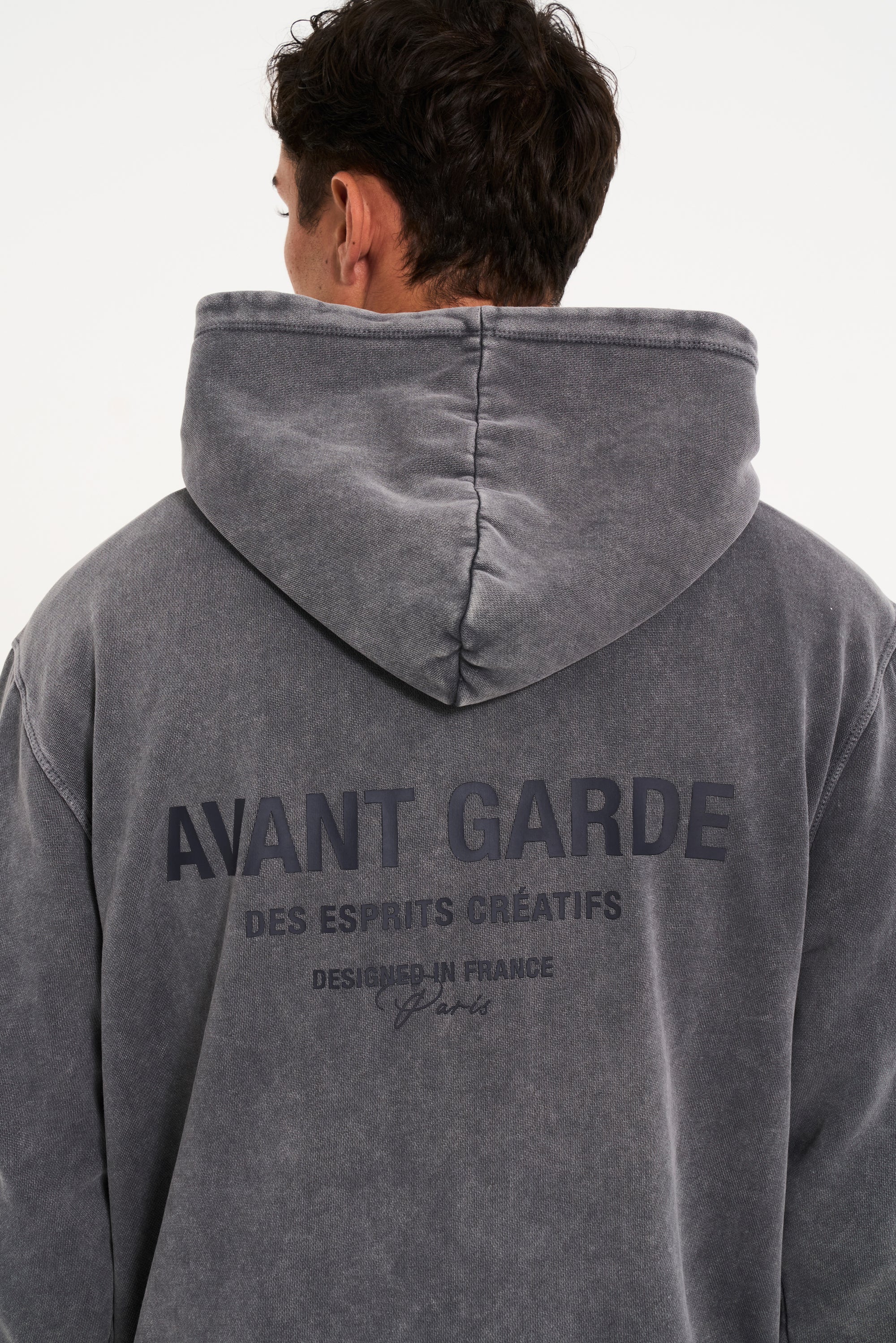 Model facing away from camera showing men's hoodie with Avant Garde writing on the back